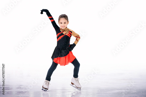 little girl figure skater in red black beautiful dress with smile skates on the ice on an indoor skating rink.