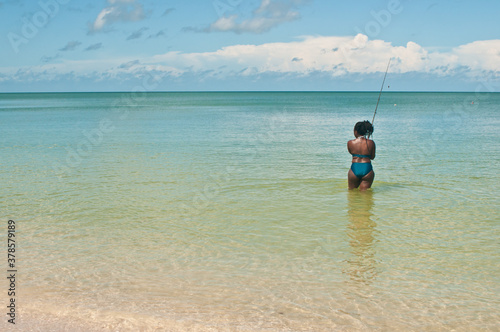 back view of a female, African Americans, wading in tropical water, fishing off a sandy beach, on the gulf of Mexico, on a sunny day