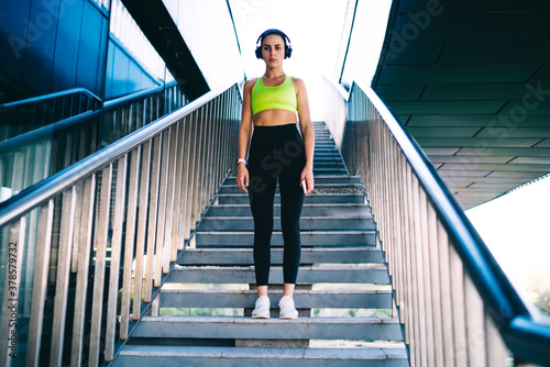 Confident young sporty sportswoman in headphones standing on stairway
