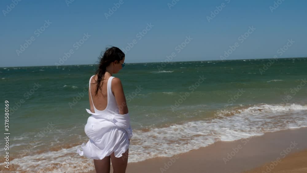 brunette woman in a white swimsuit walks along a sandy beach by the sea in summer brunette woman in a white swimsuit walks along a sandy beach by the sea in summer