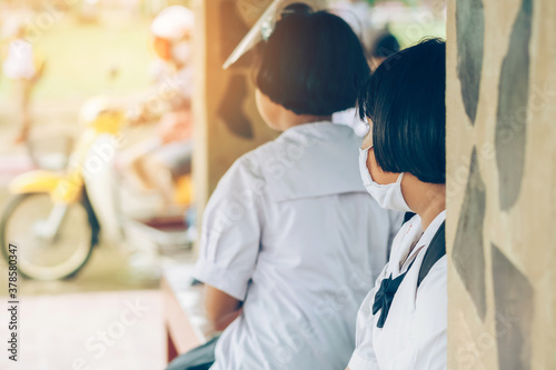 Female elementary school student wear face mask to prevent the Coronavirus(Covid-19) wait for her parents to pick her up to return home after school and the rain just stop in front of the school gate