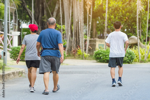 Back view portrait of a Asian elderly man in fitness wear walking and jogging for good health in public park. Senior jogger in nature. Older Man enjoying Peaceful nature. Healthcare concept.