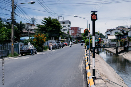​The traffice light pole with only red light on it between canal and road in the local road at Chonburi Province (East of Thailand).