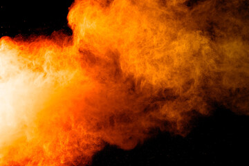 Abstract orange powder explosion. Closeup of orange dust particle splash isolated on black background.