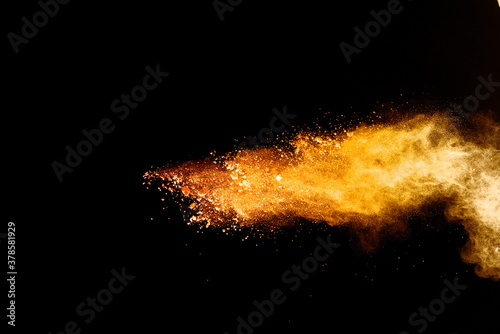 Abstract orange powder explosion. Closeup of orange dust particle splash isolated on black background.