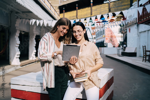 Cheerful female students enjoying friendly meeting for social networking via touch pad  happy hipster girls with education textbook using digital tablet with 4g wireless for watching web video