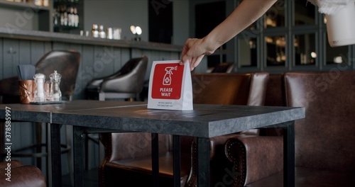 Waitress placing warning sanitizing sign on a table in a restaurant, COVID-19 pandemic, coronavirus spread preventive measures