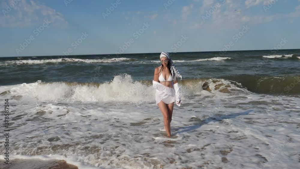 brunette woman in a white swimsuit walk along a sandy beach by the sea in summer brunette woman in a white swimsuit walk along a sandy beach by the sea in summer