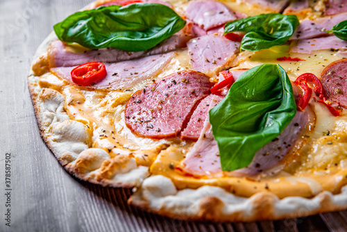 Pizza with Mozzarella cheese, ham, tomato sauce, salami, pepper, Spices and Fresh basil. Italian pizza on wooden table background