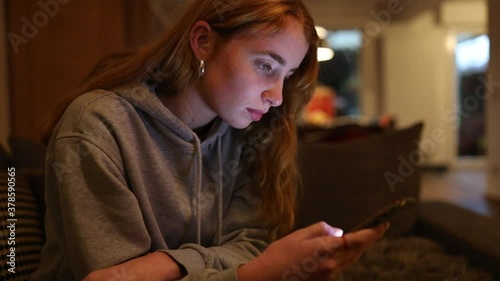 junge Frau schreibt abends mit ihrem Smartphone, das Gesicht wird dabei vom Display angeleuchtet