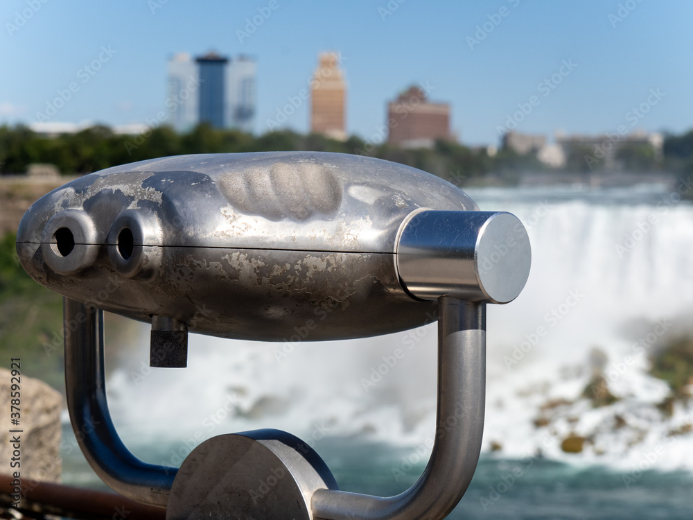 A closeup of coin operated viewing binoculars pointing at the Niagara Falls American Falls in New York USA out of focus in the distance