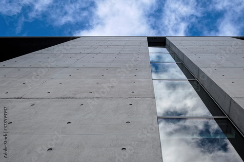 Modern building against blue cloudy sky. Bottom up view. Glass reflection and concrete facade. 