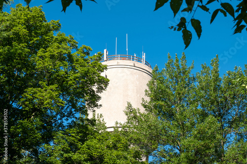 The tank of an old concrete water tower, with modern telecommunication antannae, peaks through the green tree leaves on a sunny day with clear blue sky. photo