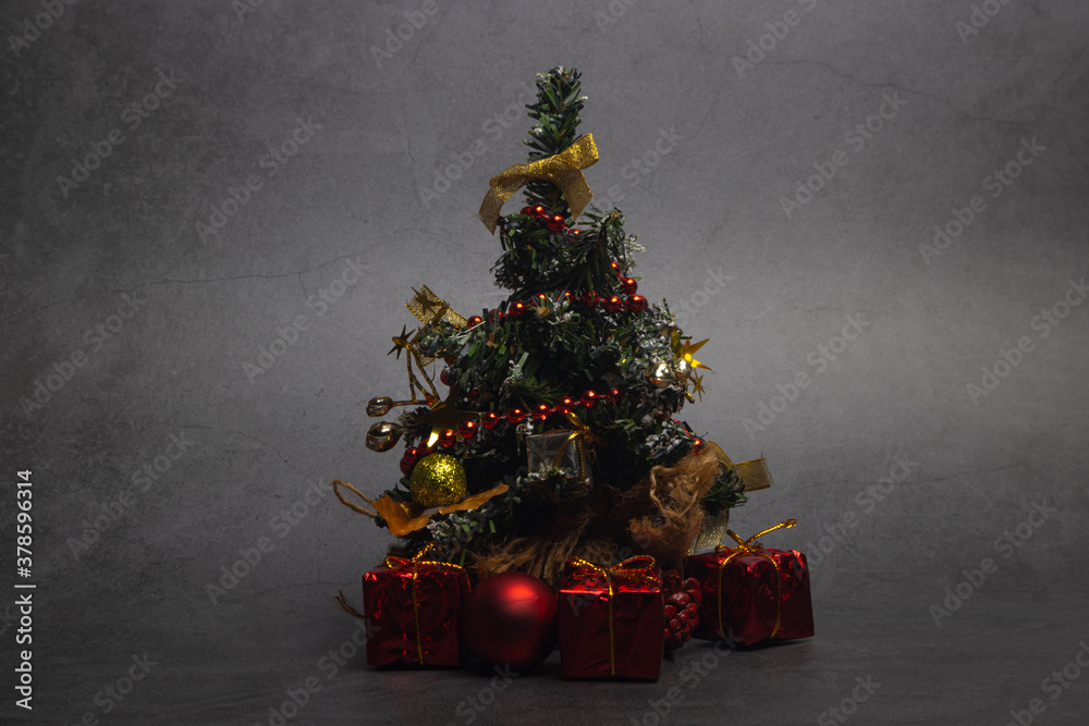 Small Christmas tree with presents and New Year's red decorations on a dark background.