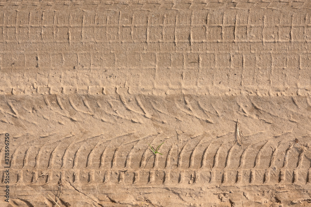 Traces of different car treads on a sandy road. There are some crumpled blades of grass. Background. Texture. Traces of different car treads on a sandy road. There are some crumpled blades of grass. Background. Texture.
