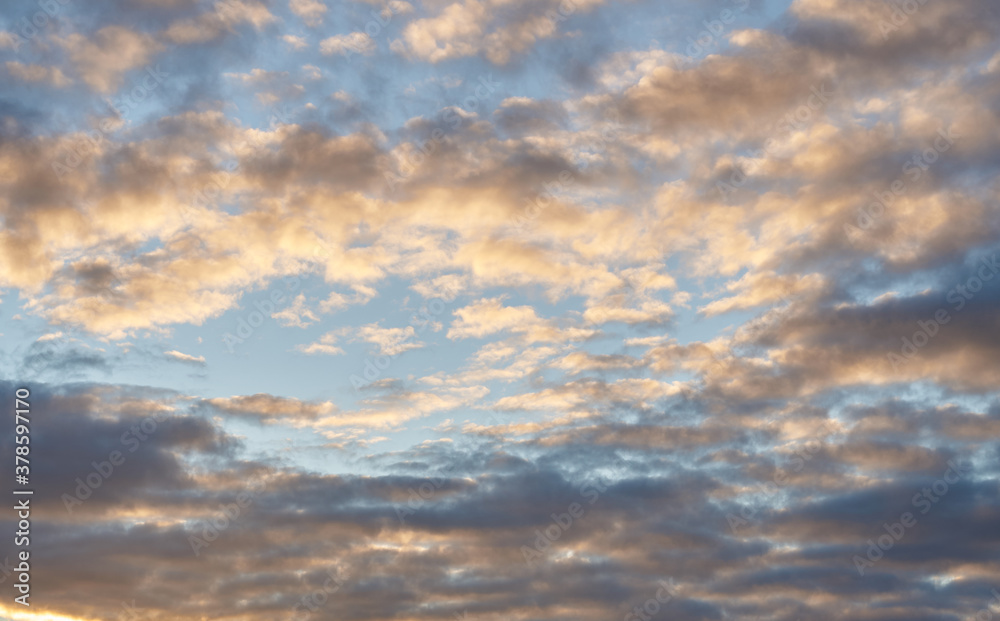 Fototapeta premium Beautiful evening blue sky at sunset with flaming bright light clouds. A warm summer evening at sunset.