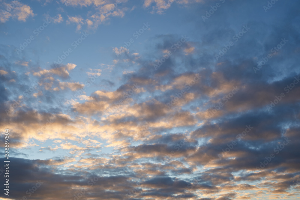 Fototapeta premium Beautiful evening blue sky at sunset with flaming bright light clouds. A warm summer evening at sunset.