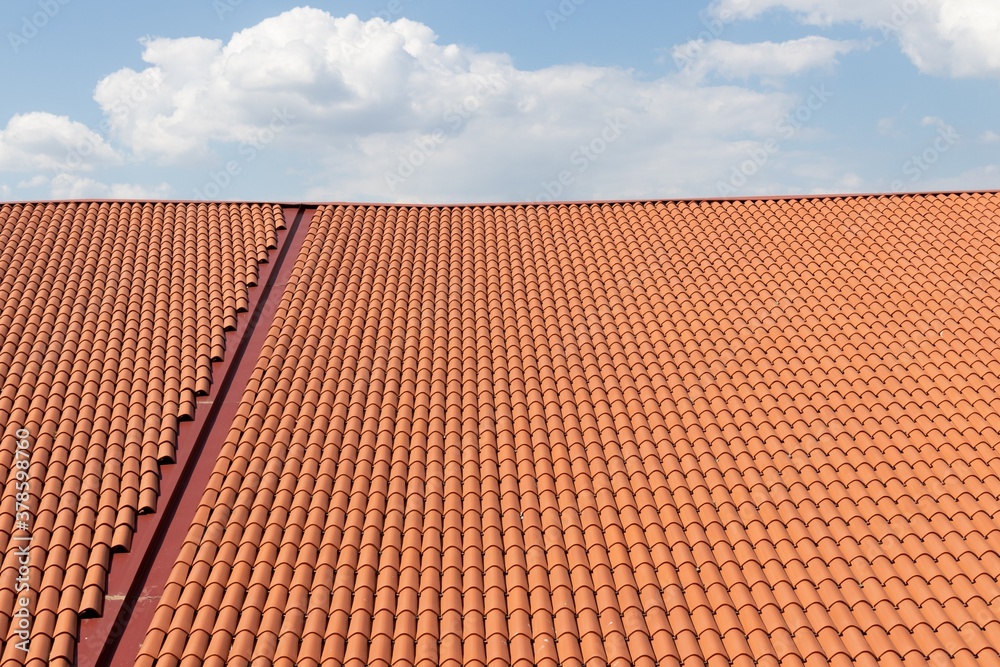Naklejka premium Wide roof covered with modern new orange tiles on a sunny day against a sky with clouds