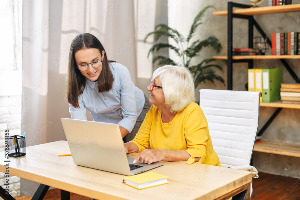 Young manager boss checking work of older female trainee, looking at computer screen in office. Youthful mentor is teaching senior female intern Young manager boss checking work of older female trainee, looking at computer screen in office. Youthful mentor is teaching senior female intern