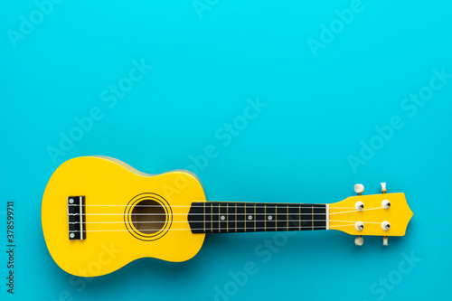 Overhead photo of ukulele with copy space. Yellow colored wooden ukulele guitar on the turquoise blue background. photo