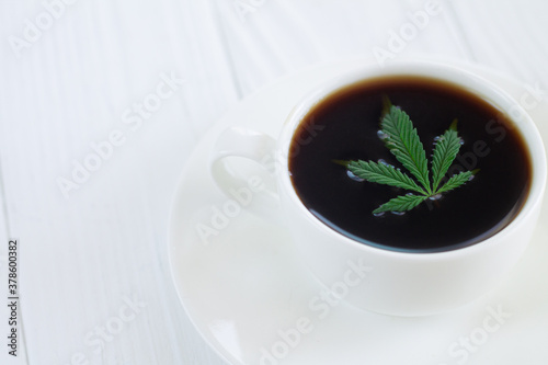 White cup of cannabis coffee with hemp leaves close-up