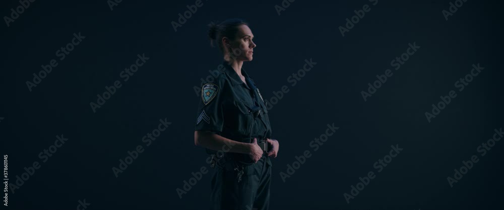 FIXED Portrait of Caucasian female police officer posing against dark background, looking into camera FIXED Portrait of Caucasian female police officer posing against dark background, looking into camera