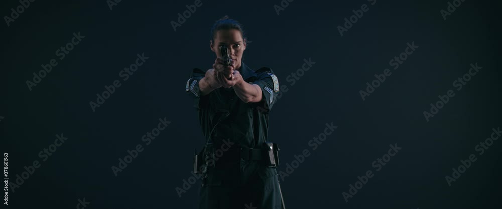 Caucasian female police officer drawing handgun from holster against dark background. Shot on RED cinema camera Caucasian female police officer drawing handgun from holster against dark background. Shot on RED cinema camera