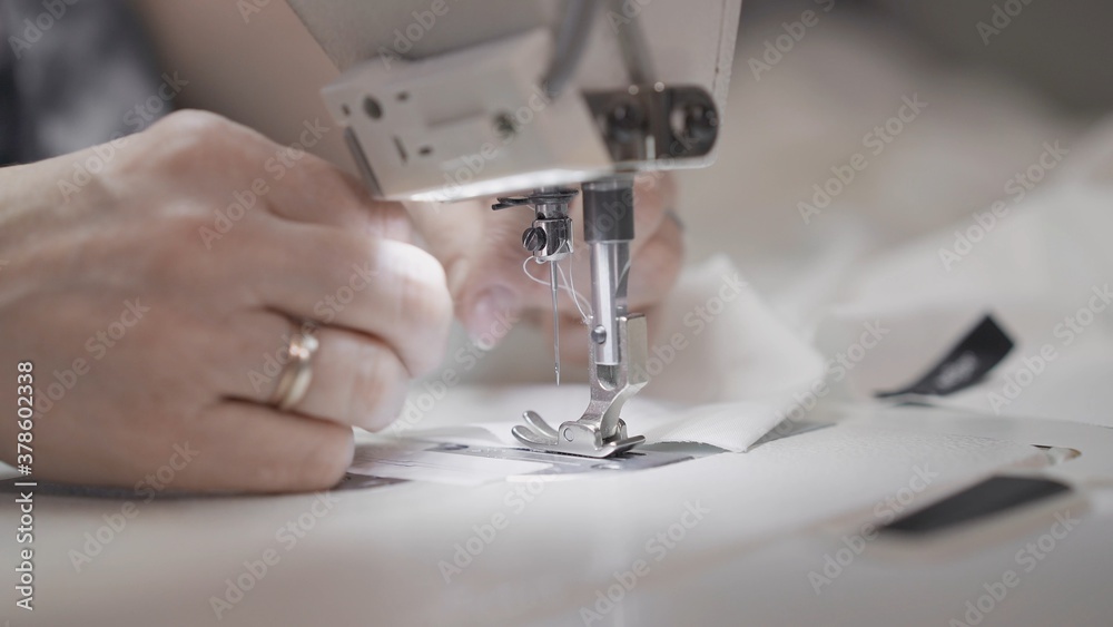 Sewing white cloth on a white sewing machine close up. Concept of sewing in modern bright studio, female hands sewing a white cloth, selective focus