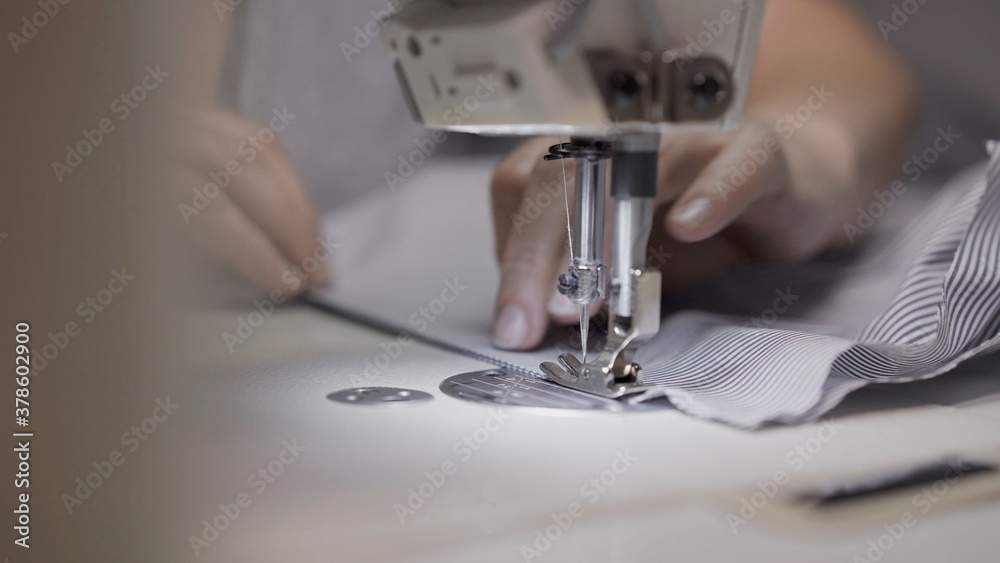 Sewing striped shirt on a white sewing machine close up. Concept of sewing in modern bright studio, female hands sewing a striped cloth, selective focus