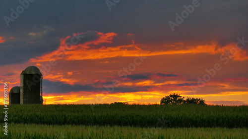 Fototapeta Naklejka Na Ścianę i Meble -  Bright Red Sunset over Corn Field with Silos. High quality photo. Red and Orange Clouds