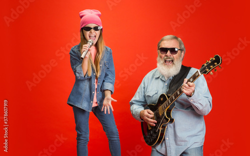 Cheerful musician. Senior man spending happy time with granddaughter in neon. Joyful elderly lifestyle, family, childhood, tech concept. Enjoying modern music, technologies. Copyspace.