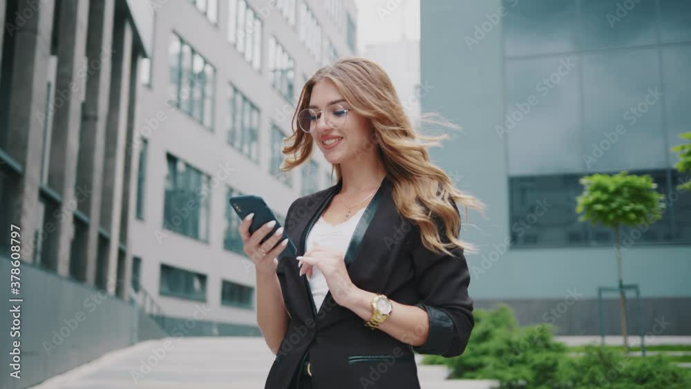Happy successful businesswoman with glasses use phone walking near business center. Internet chatting. Digital girl worker. Corporate entrepreneur. Street. Online. Stylish. Close up. Slow motion. Happy successful businesswoman with glasses use phone walking near business center. Internet chatting. Digital girl worker. Corporate entrepreneur. Street. Online. Stylish. Close up. Slow motion.