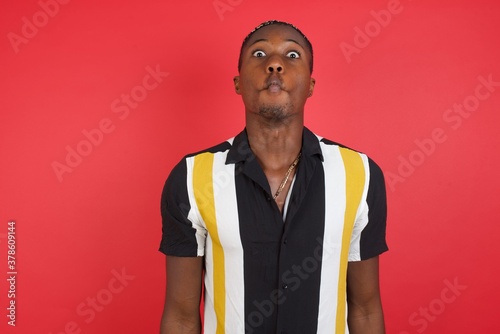 African american man with braids wearing casual shirt over isolated red background making fish face with lips, crazy and comical gesture. Funny expression.