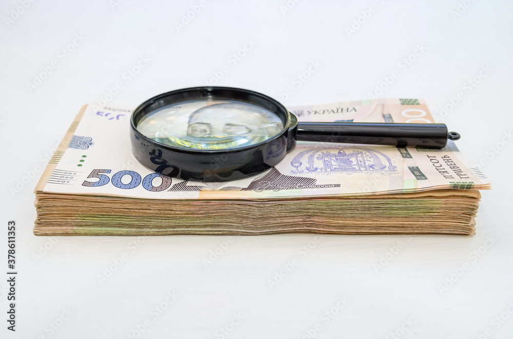 Stack of hryvnia banknotes and a magnifying glass. Light background. A lot of money. Ukrainian hryvnia. Stack of hryvnia banknotes and a magnifying glass. Light background. A lot of money. Ukrainian hryvnia.