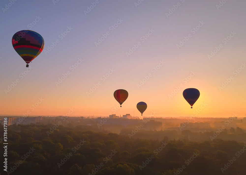 Aerial drone view of colorful hot air balloons flying over green park and river in small european city at summer sunrise Aerial drone view of colorful hot air balloons flying over green park and river in small european city at summer sunrise