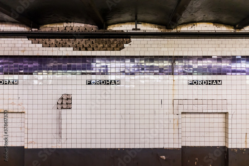Empty subway station platform in underground transit in NYC Bronx Fordham Road Heights with sign on tiled wall peeling