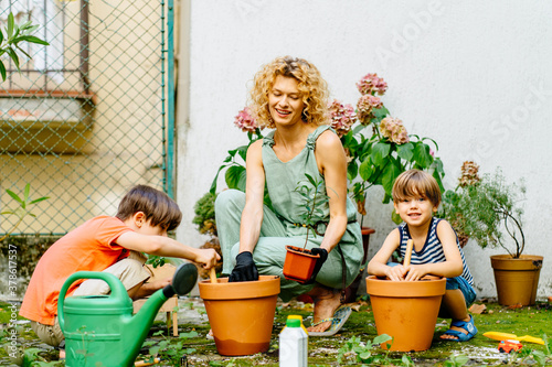 Family having fun outdoor. Two children in the garden and learning to plant flowers in pots with their mother. Family together creating cozy courtyard. Developmental activities for children concept.