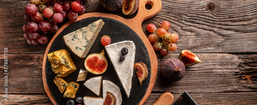 Delicious gourmet cheese, assortment of soft cheeses served with sliced sweet fresh figs and grapes on a rustic wooden background, catering, banner, menu, recipe, place for text