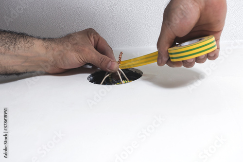 An electrician twists the wires with yellow-green duct tape. Installation of the electricity distribution box.