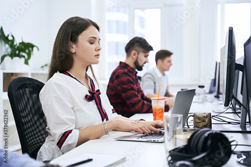People working in modern IT office. Group of young and experienced programmers and software developers sitting at desks working on computers. Team at work. High quality image.