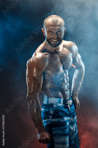 Handsome strong bodybuilder posing in studio on black background.