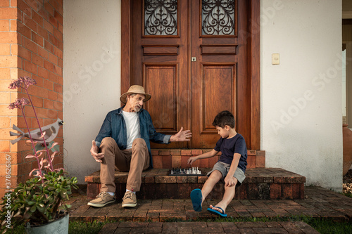 Garoto joga de xadrez com seu avô na escada de casa.