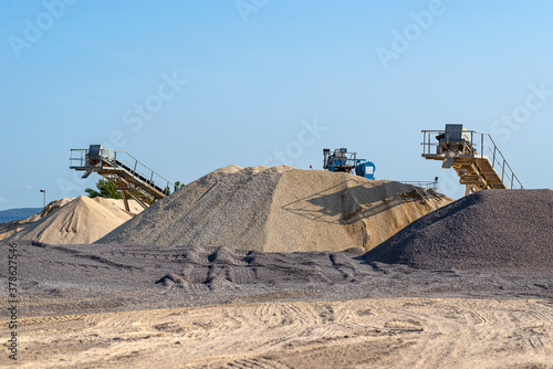 Conveyor belt over heaps of gravel against the blue sky at an industrial cement plant.