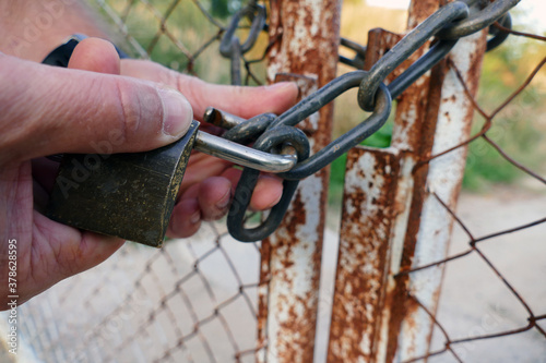 A male hand unlocks a lock on a rusty gate from an old fence