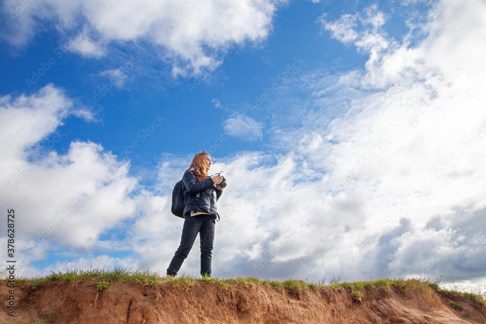 a tourist girl with a backpack and a camera walks along the river Bank on a Sunny day, taking pictures of the landscape, autumn a tourist girl with a backpack and a camera walks along the river Bank on a Sunny day, taking pictures of the landscape, autumn