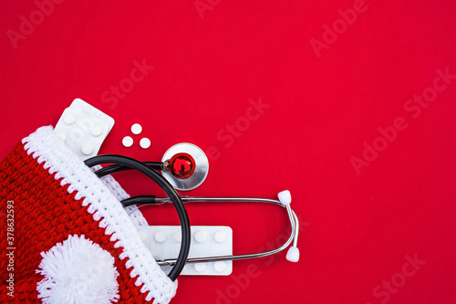 Medical banner 2021 for clinics with pills, stethoscope and Christmas haton a red background. Copyspace. Medicine new year flatlay. photo