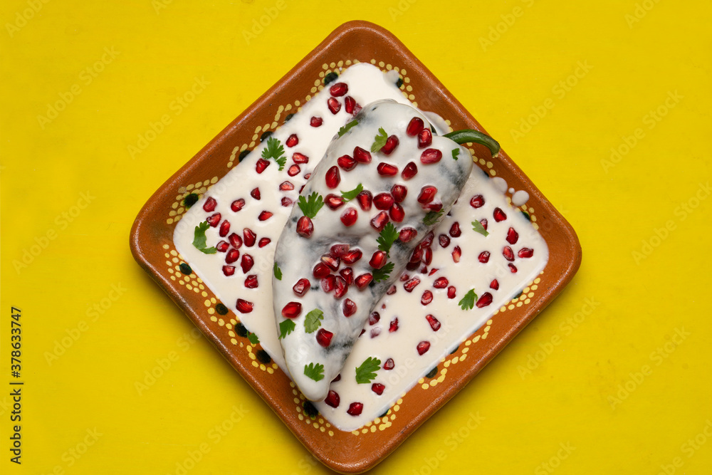 Fototapeta premium Mexican stuffed poblano peppers also called nogada with pomegranate on yellow background