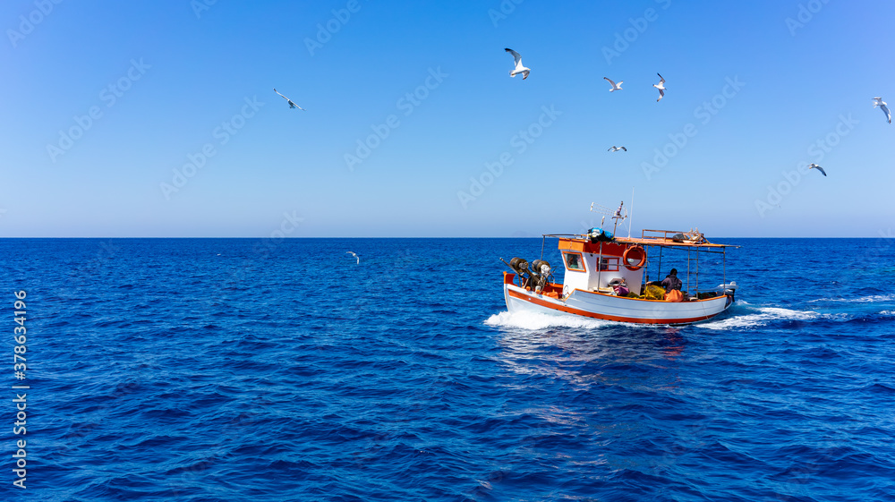 Orange and white fishing boat followed by seagulls on aegean sea. blue sky and sunny day