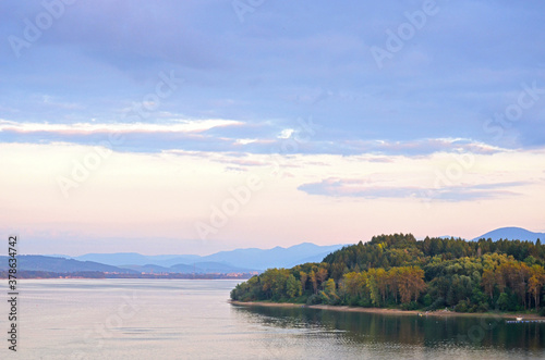 Autumn landscape of a lake shore with colorful trees and blue mountains in the background on sunset