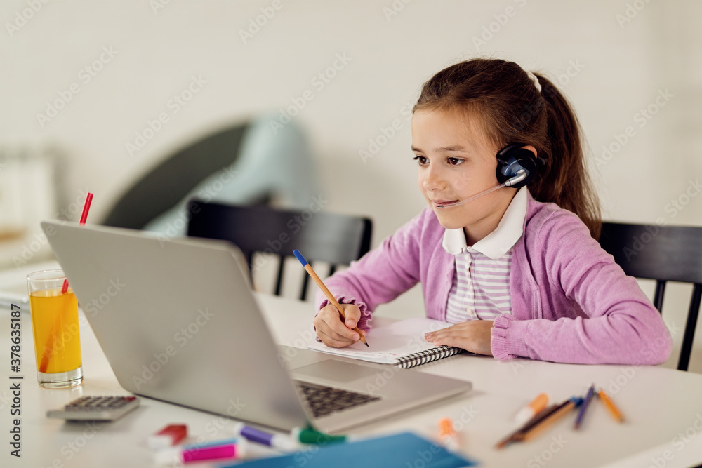 Cute girl writing notes while e-learning over laptop at home. Cute girl writing notes while e-learning over laptop at home.